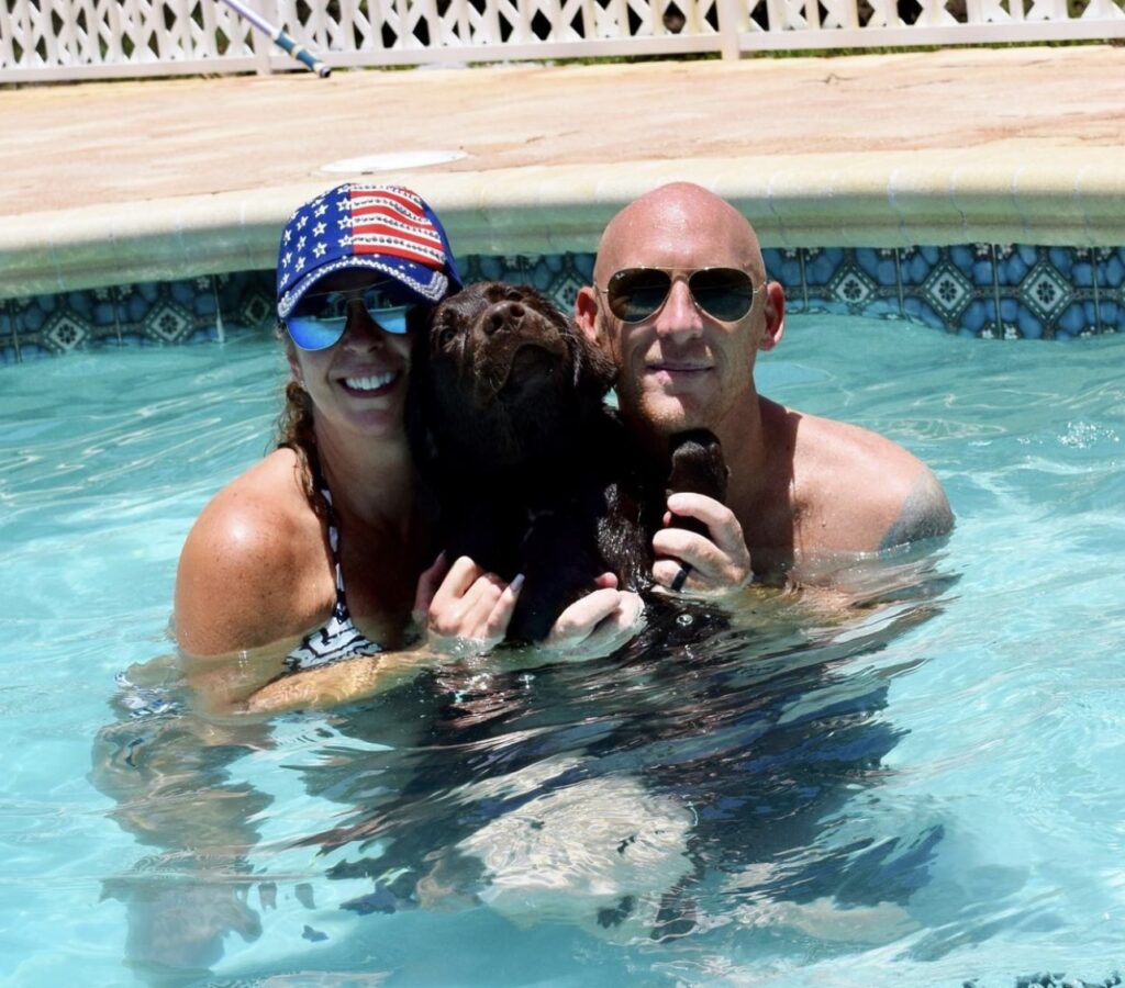 A couple taking a swim in swimming pool with their dog